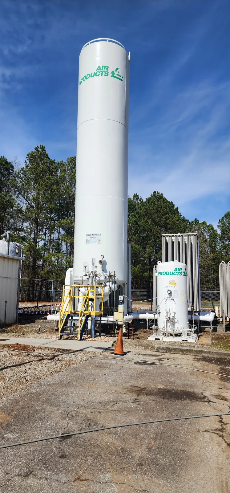Tall white industrial storage tank after pressure washing, with a catwalk, piping, and a clean shell.